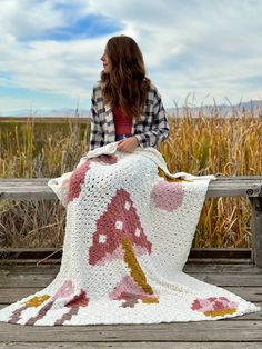 a woman is sitting on a bench with a crocheted blanket draped over her