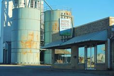 an old industrial building sits in the middle of a street next to some silos