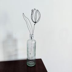 a glass vase with flowers in it sitting on a wooden table next to a white wall