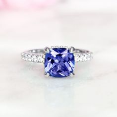 Gorgeous Hidden Halo Cushion Tanzanite Ring ►Made of solid sterling silver with rhodium finish (925) ►Accented With Simulated Diamonds (CZ) ►Average band width: 2.1mm Center Stone: Tanzanite Shape: Cushion Gemstone Creation: Simulated Measurements: 7.0 x 7.0 mm Carat Weight: 2ct (approx.) Hardness: 8 (Mohs scale) ►Matching band is sold separately: https://www.etsy.com/listing/879526036/2mm-diamond-wedding-band-half-eternity?ref=shop_home_active_15&pro=1&frs=1 ✓ 100% Nickel-Free ✓ Hypoall Classic Tanzanite Diamond Ring With Prong Setting, Classic Tanzanite Diamond Ring For Promise, Timeless Tanzanite Promise Ring, Classic Tanzanite Ring With Center Stone, Classic Tanzanite Wedding Ring With Prong Setting, Classic Tanzanite Cushion Cut Rings, Classic Tanzanite Birthstone Ring For Wedding, Classic Tanzanite Jewelry, Classic Tanzanite Solitaire Ring