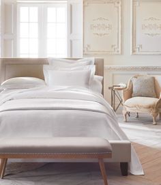 a bed with white sheets and pillows in a room next to two chairs on the floor