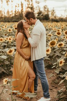 a pregnant couple kissing in a field of sunflowers