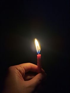 a hand holding a lit candle in the dark with one light on it's end