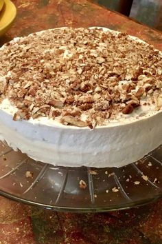 a cake sitting on top of a glass platter covered in frosting and nuts