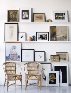 two wicker chairs sitting next to each other in front of a wall with pictures on it