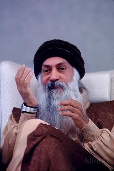 an old man with a long white beard sitting in a chair and holding his hand up