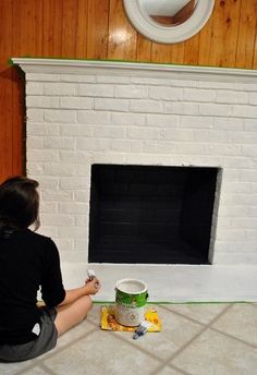 a woman sitting on the floor painting a fireplace