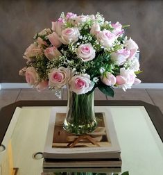 a vase filled with pink and white flowers on top of a table next to a stack of books