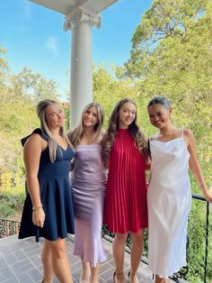 four women in dresses posing for a photo on a porch with trees in the background