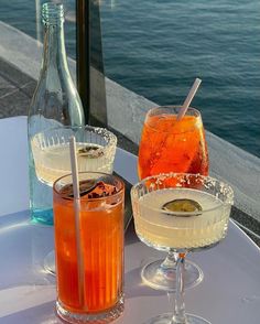 two drinks are sitting on a table next to each other with water in the background