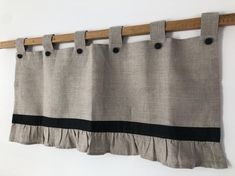 the curtain is hanging on the wall with two black pins and one white stripe, along with a wooden rod