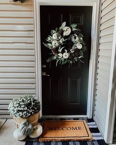 a welcome mat and potted plants on the front porch with a black door in the background