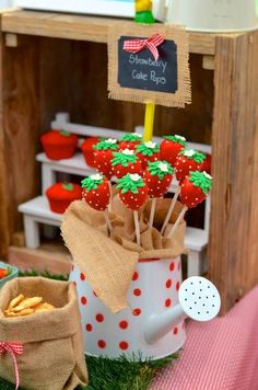 strawberries are arranged on sticks in a teapot and placed next to other items