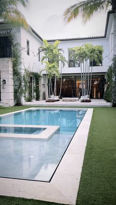 an empty swimming pool in front of a large white house with palm trees around it