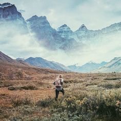 a woman walking through a field with mountains in the background