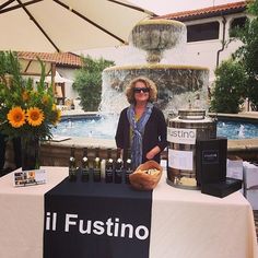 a woman standing behind a table with bottles on it and an umbrella in the background