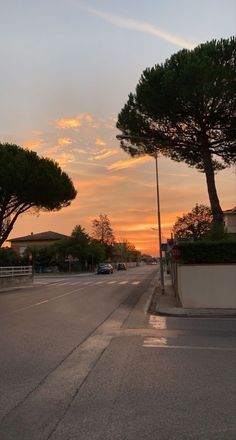 the sun is setting behind some trees on the side of the road in an empty street