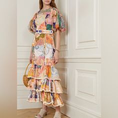 a woman standing in front of a white wall wearing a multicolored dress with ruffles