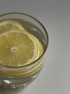 a glass filled with liquid and sliced lemon wedged into it's sides, on a white surface