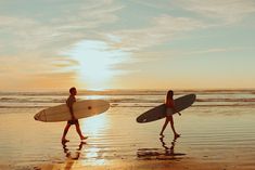 two people walking on the beach with surfboards