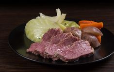 a black plate topped with meat and veggies on top of a wooden table