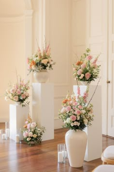 three white vases filled with flowers on top of a wooden floor