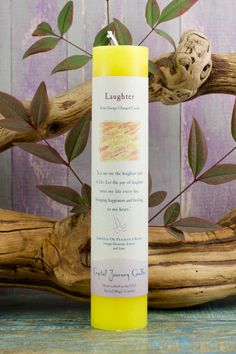 a yellow candle sitting on top of a wooden table next to some branches and leaves