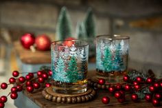 two glasses filled with liquid sitting on top of a wooden table next to christmas decorations