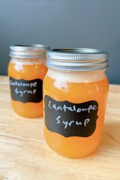 two jars filled with orange liquid sitting on top of a wooden table next to each other