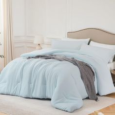 a bed with blue sheets and pillows in a white room next to a lamp on a table