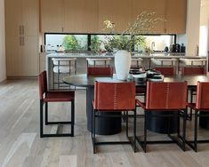 a dining room table with red chairs and a white vase on it's center