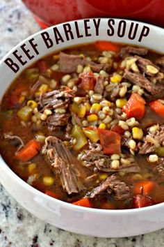 a bowl of beef barley soup with corn and carrots in it on a table