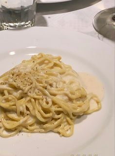 a white plate topped with pasta covered in gravy next to a glass of water