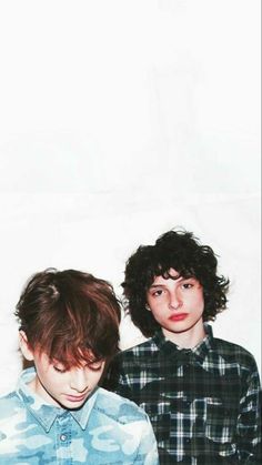 two young men standing next to each other in front of a white wall and looking at the camera