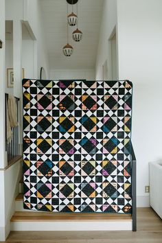 a black and white quilt is hanging on the wall next to some stairs in a house