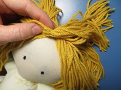 a hand holding a yellow string wrapped stuffed animal