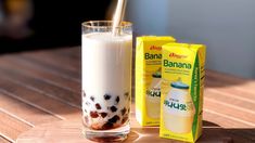 a glass filled with milk sitting on top of a wooden table next to a carton of milk