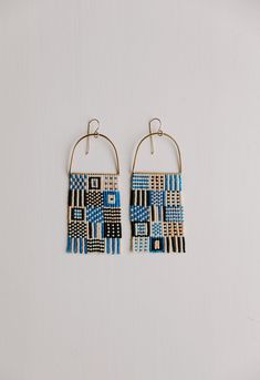 two pairs of earrings with blue and white designs on them hanging from gold hoops