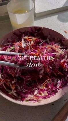 a bowl filled with shredded red cabbage next to a glass of milk and utensils