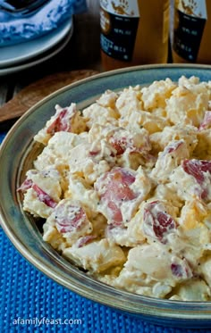 a bowl full of potato salad next to two bottles of beer on a table with blue place mats