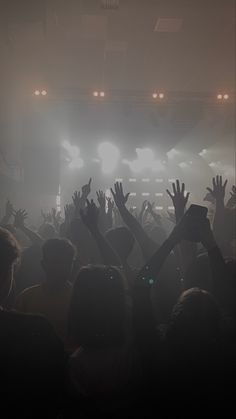 a crowd of people at a concert with their hands in the air and lights on