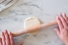 two hands are rolling dough on a marble counter top, while another hand is holding a rolling pin