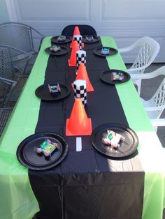 a table set up with black plates and orange traffic cones on top of green cloth