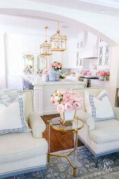 a living room filled with white furniture and pink flowers on top of a coffee table