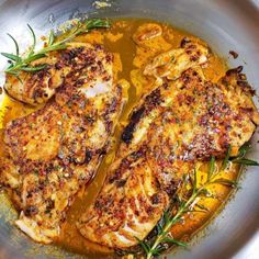 two pieces of chicken are in a pan with lemons and herbs on the side