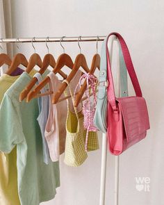 several different colored shirts hanging on a clothes rack with a handbag in the foreground