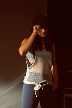 a woman standing in the dark with her hand on her head and wearing a hat