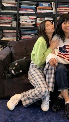 two women sitting on a couch in front of a bookshelf