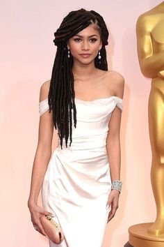 a woman in a white dress standing next to an oscars statue with her hand on her hip