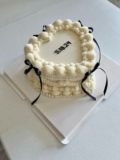 a cake with white frosting and black ribbon on top is sitting on a table